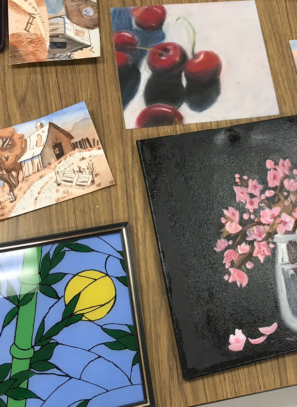 Five different paintings showcased laying on top of a table