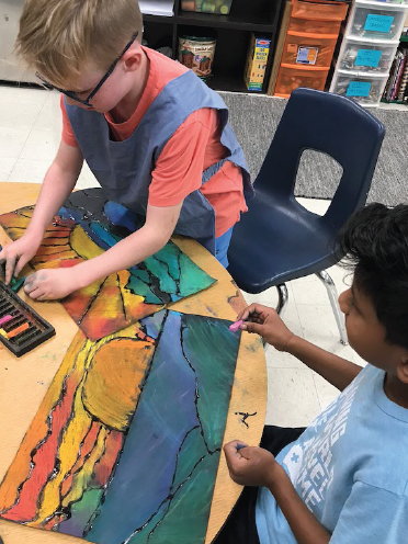 2 students on a table finishing their painting projects