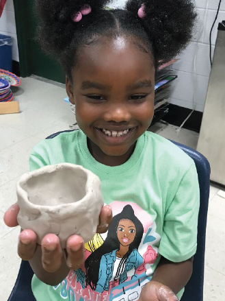 a little student showing her pottery project on her hand