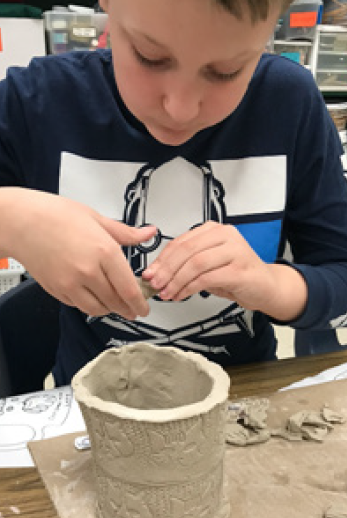 a concentrated little student boy working on his pottery project