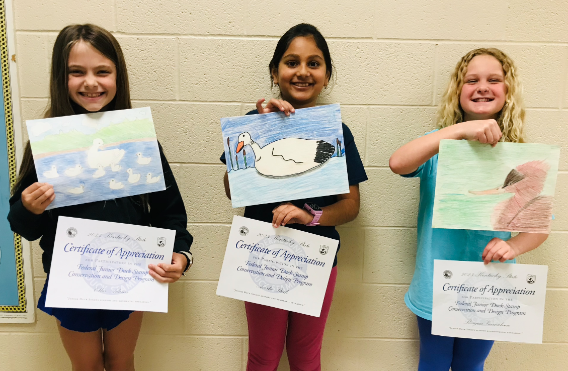 three student girls showing their paintings and certificates for their good work