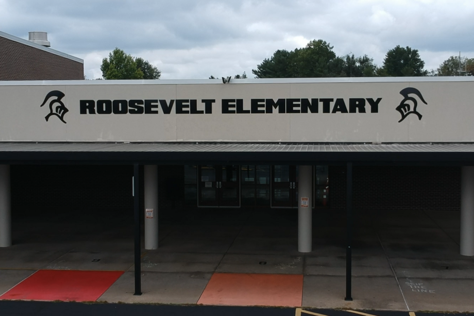 Entrance to Roosevelt Elementary. White roof with black trim and a red and orange carpet on the front.