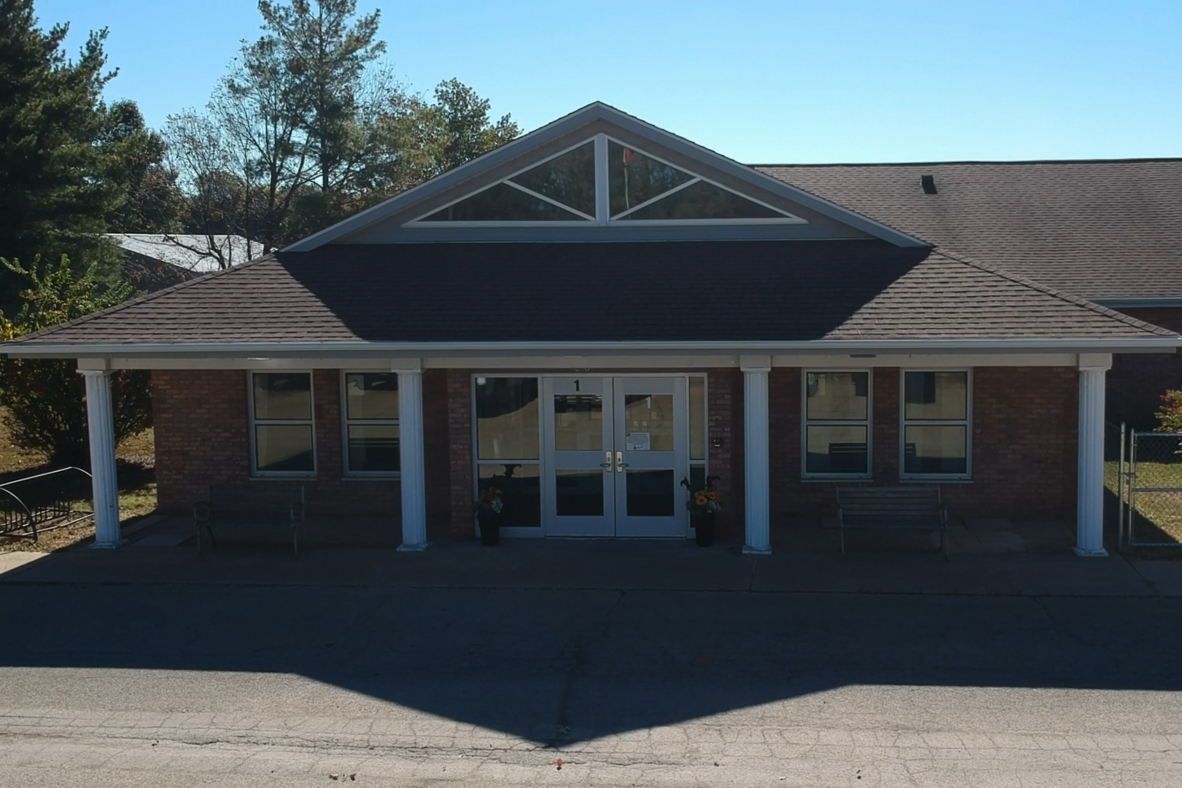 A single-story brick building with a triangular roof and a gray shade. It has large glass doors.