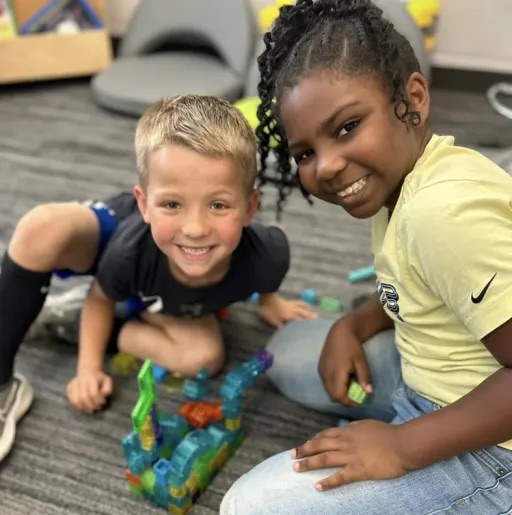 boy and a gilr smiling at the camera while sitting on the floor 