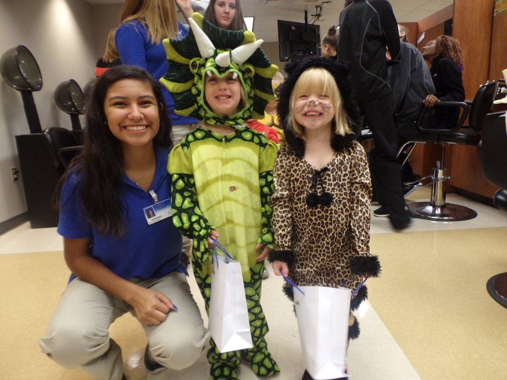 Two teachers and a student wearing a dinosaur costume posing for photo