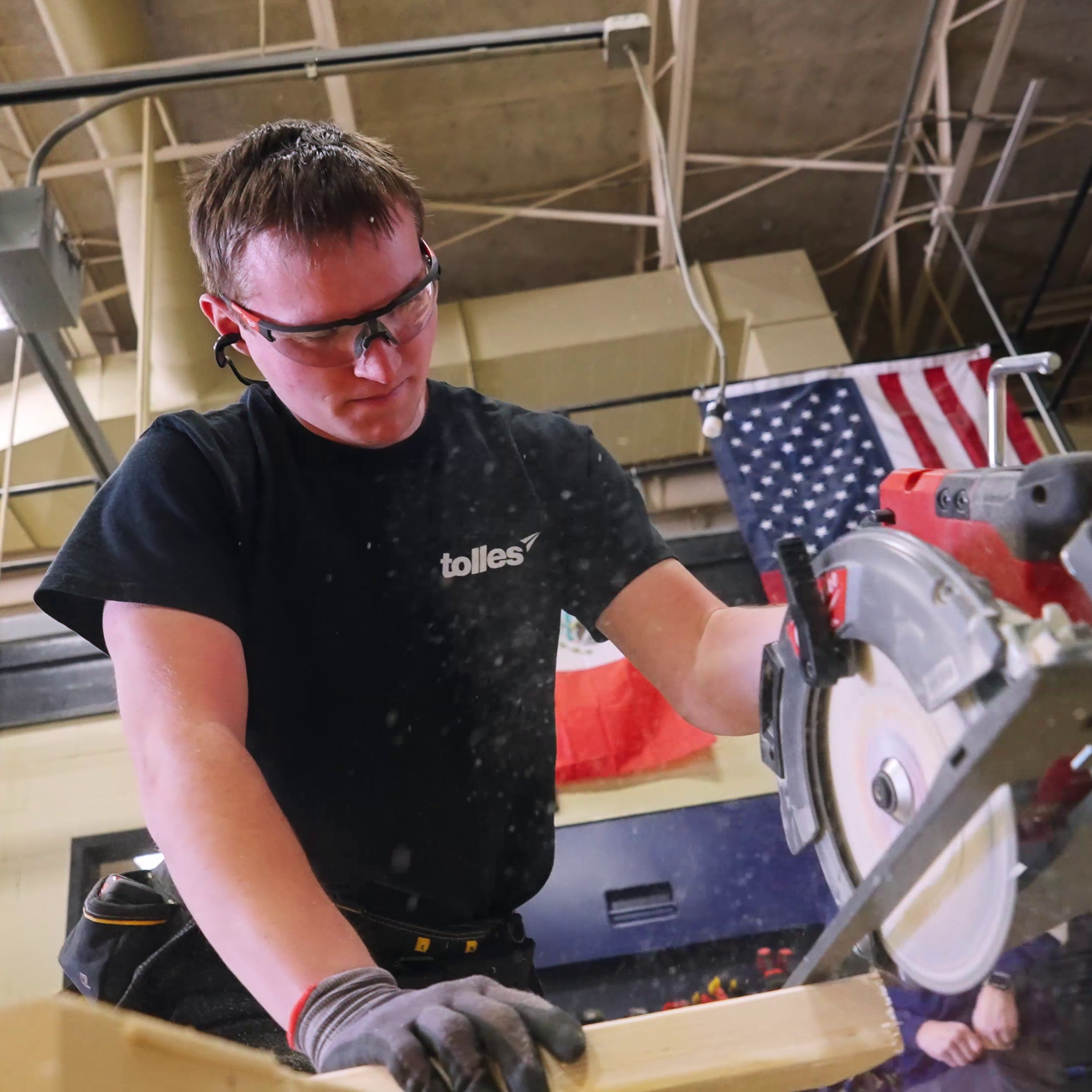 A man in a workshop wearing protective gear uses a saw to cut a wooden plank.