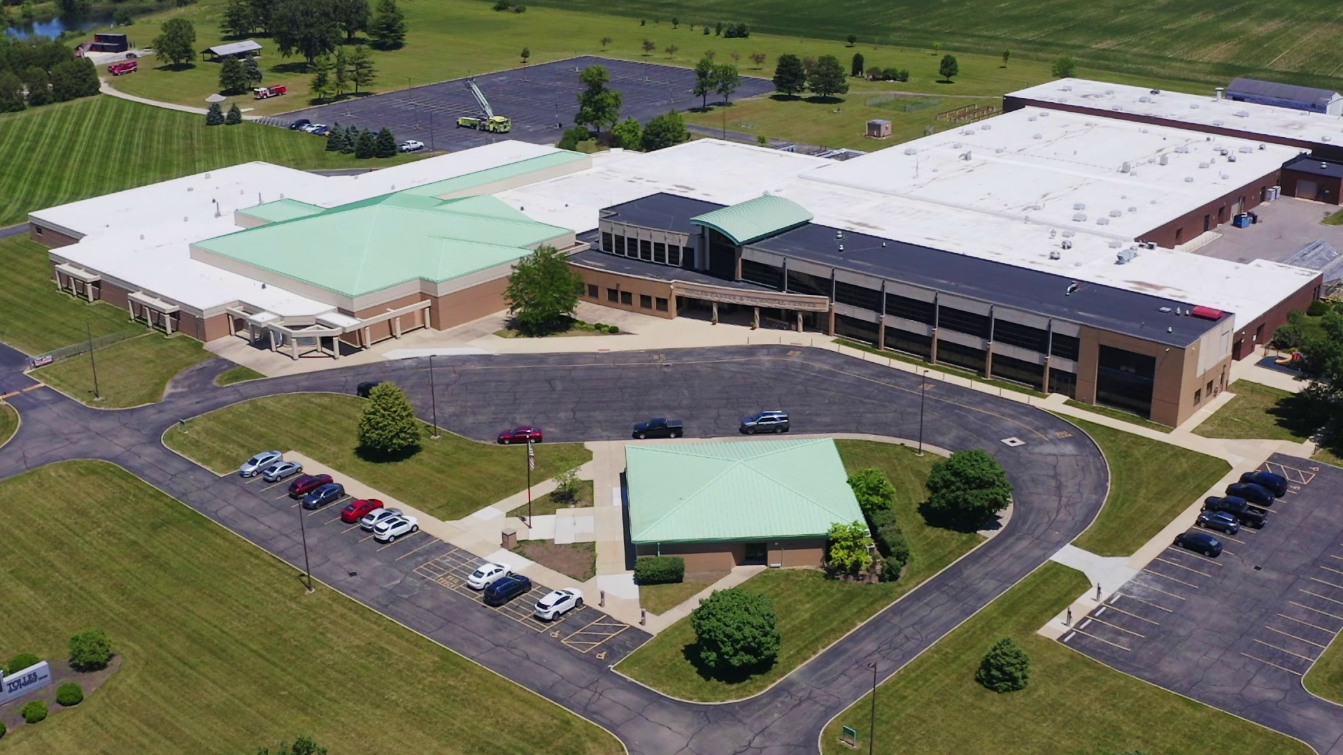 Aerial view of a large building with green roofs, surrounded by a parking lot with several cars parked.