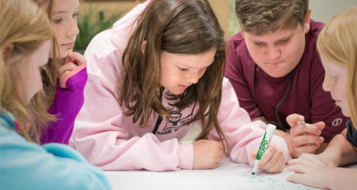 A kid writing on a piece of paper while other people watch