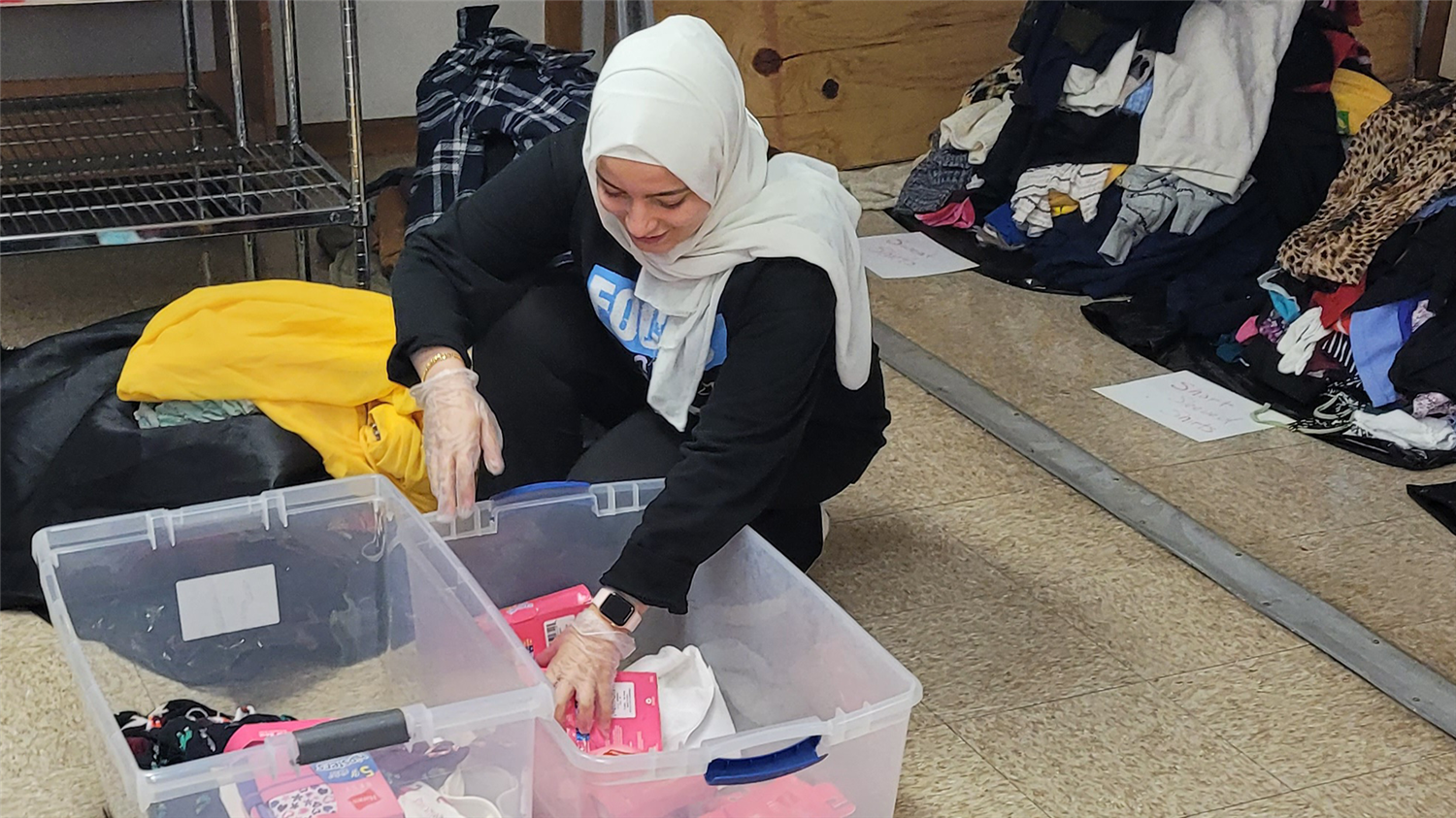 A person in a hijab is organizing and sorting items on a table. They are reaching into a bin of items