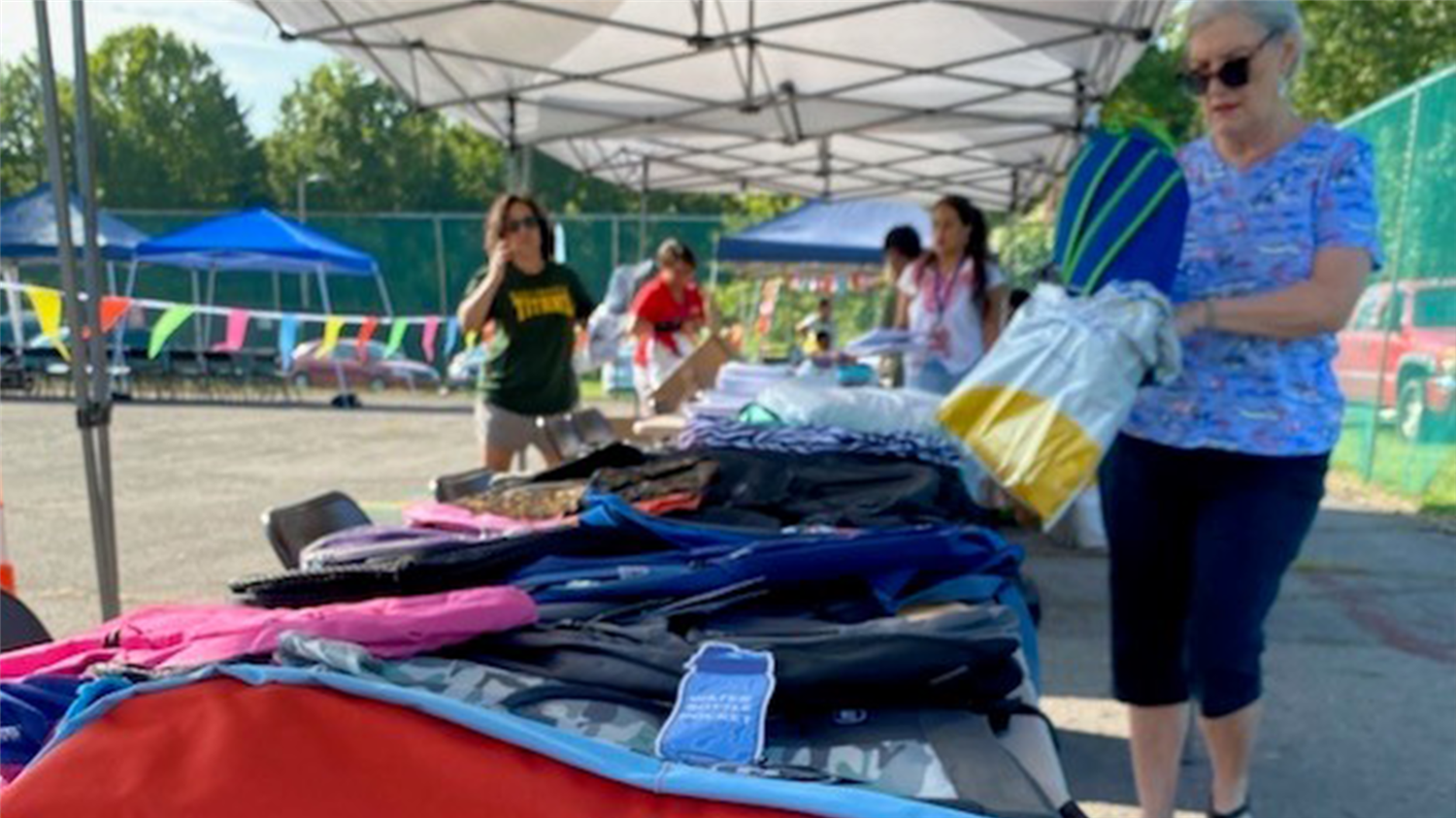 A woman at an outdoor table with a variety of colorful sports equipment and clothing.