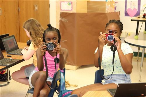 2 girls sitting on chairs holding a camera