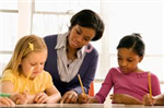 2 girls writing and a teacher looking at them