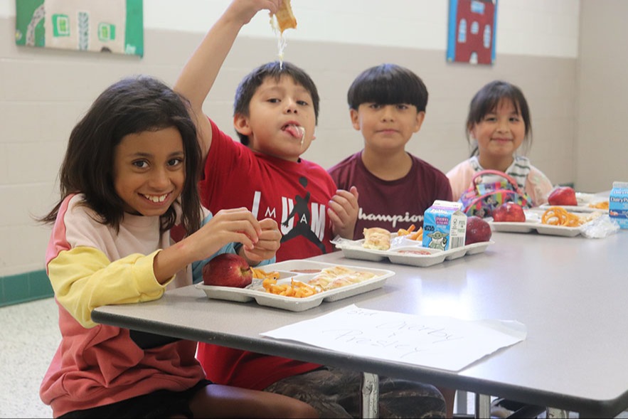 students sitting at the lunch table, talking, smiling and eating