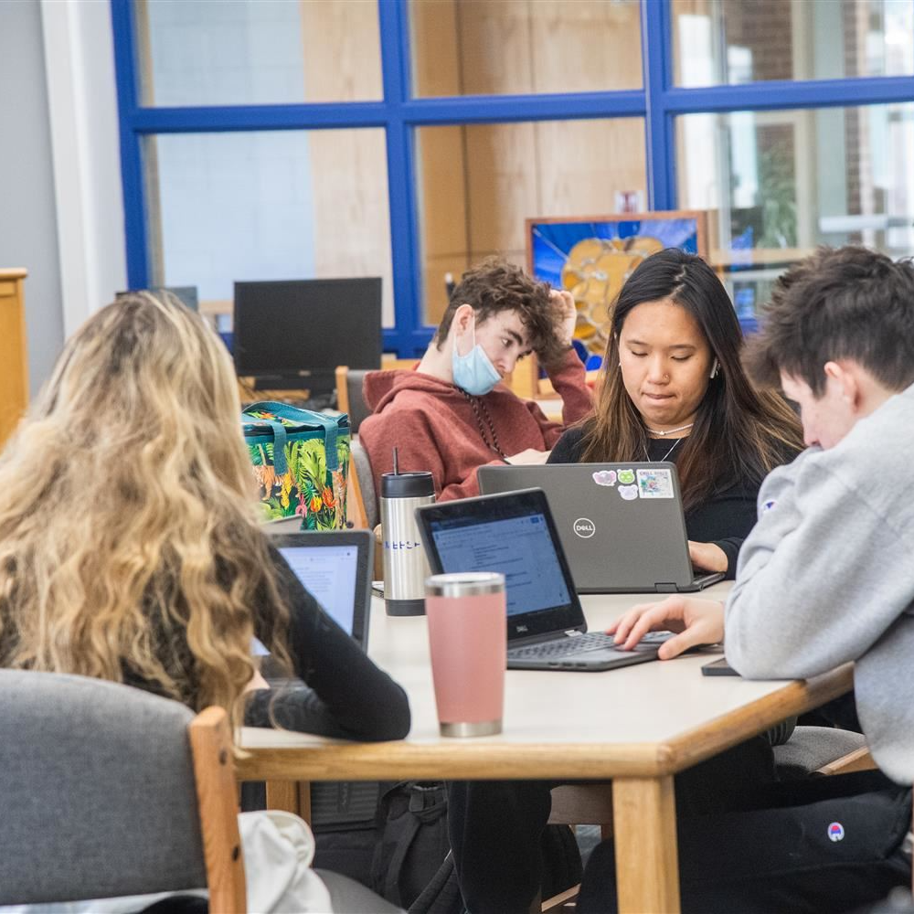 group of high school students on a table working on their computers