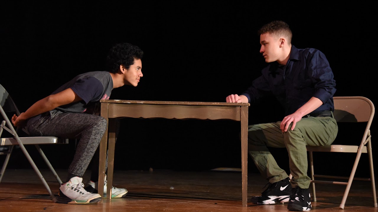 Two teens at acting class sitting on a table.