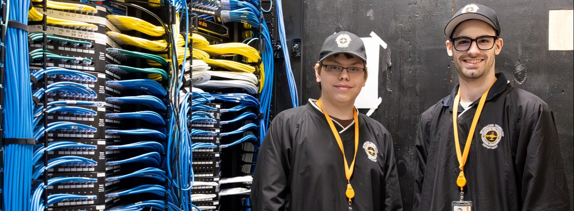 Two IT workers stand near a network port.