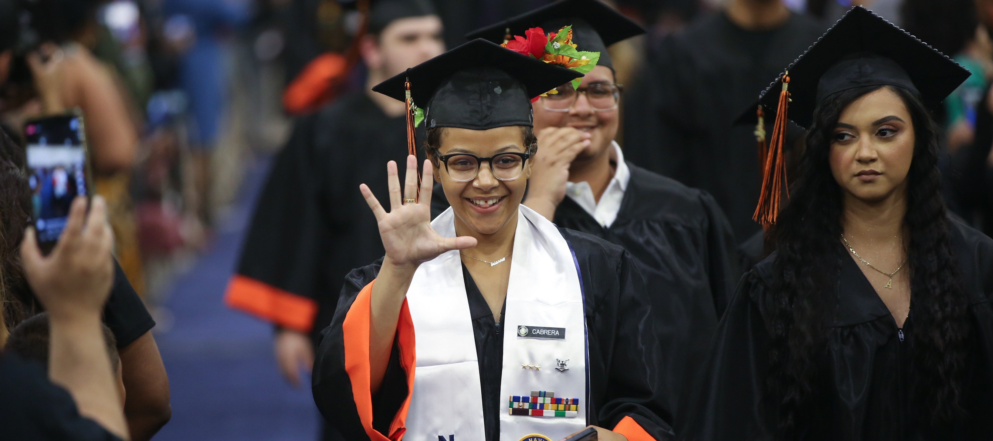 Student in cap and gown waves during graduation ceremony