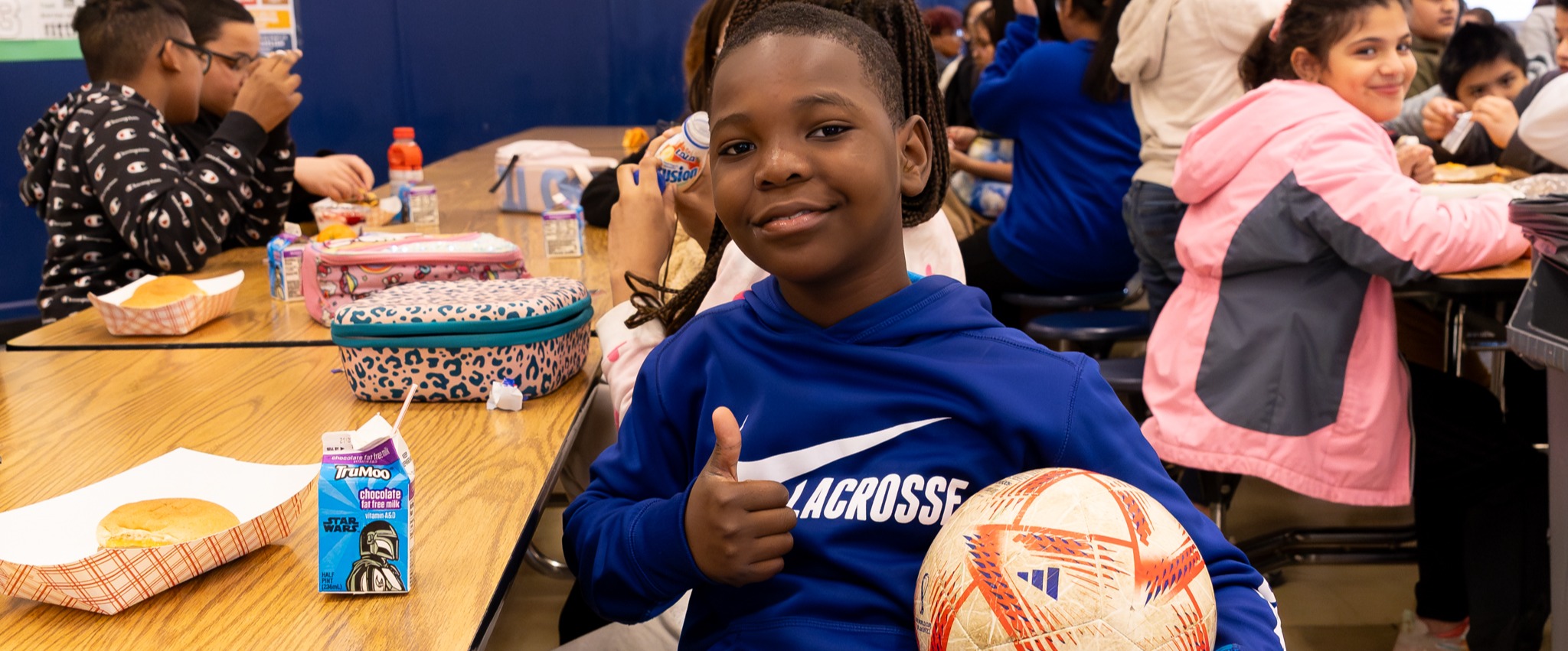 A boy holding a soccer ball and giving a thumbs up