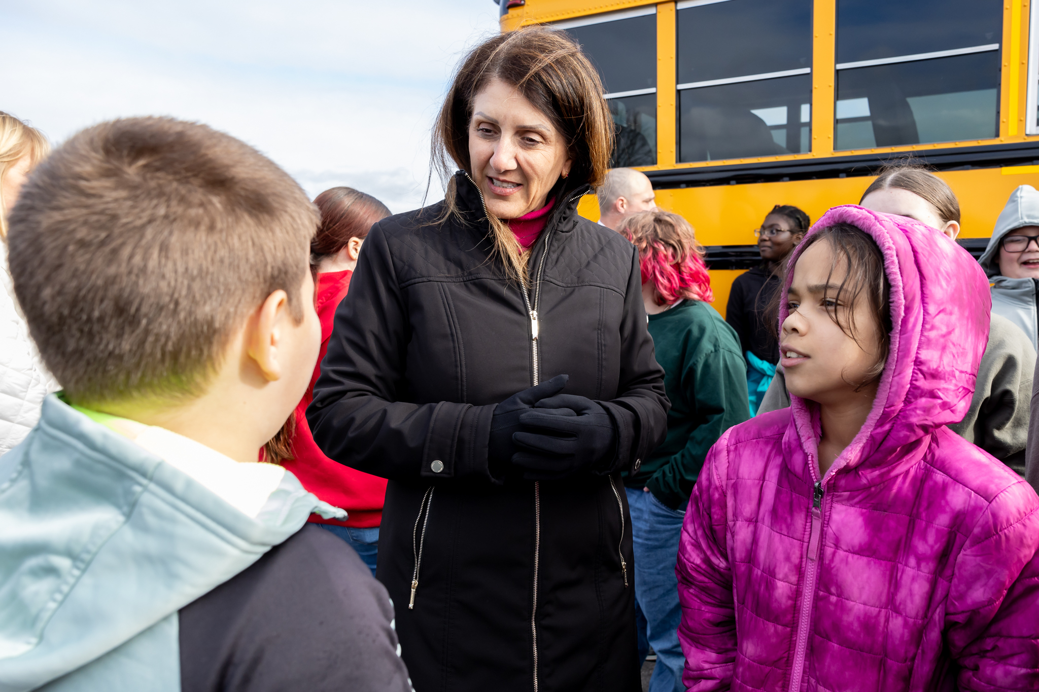 Superintendent Rachel Monárrez speaks with students next to an electric school bus.