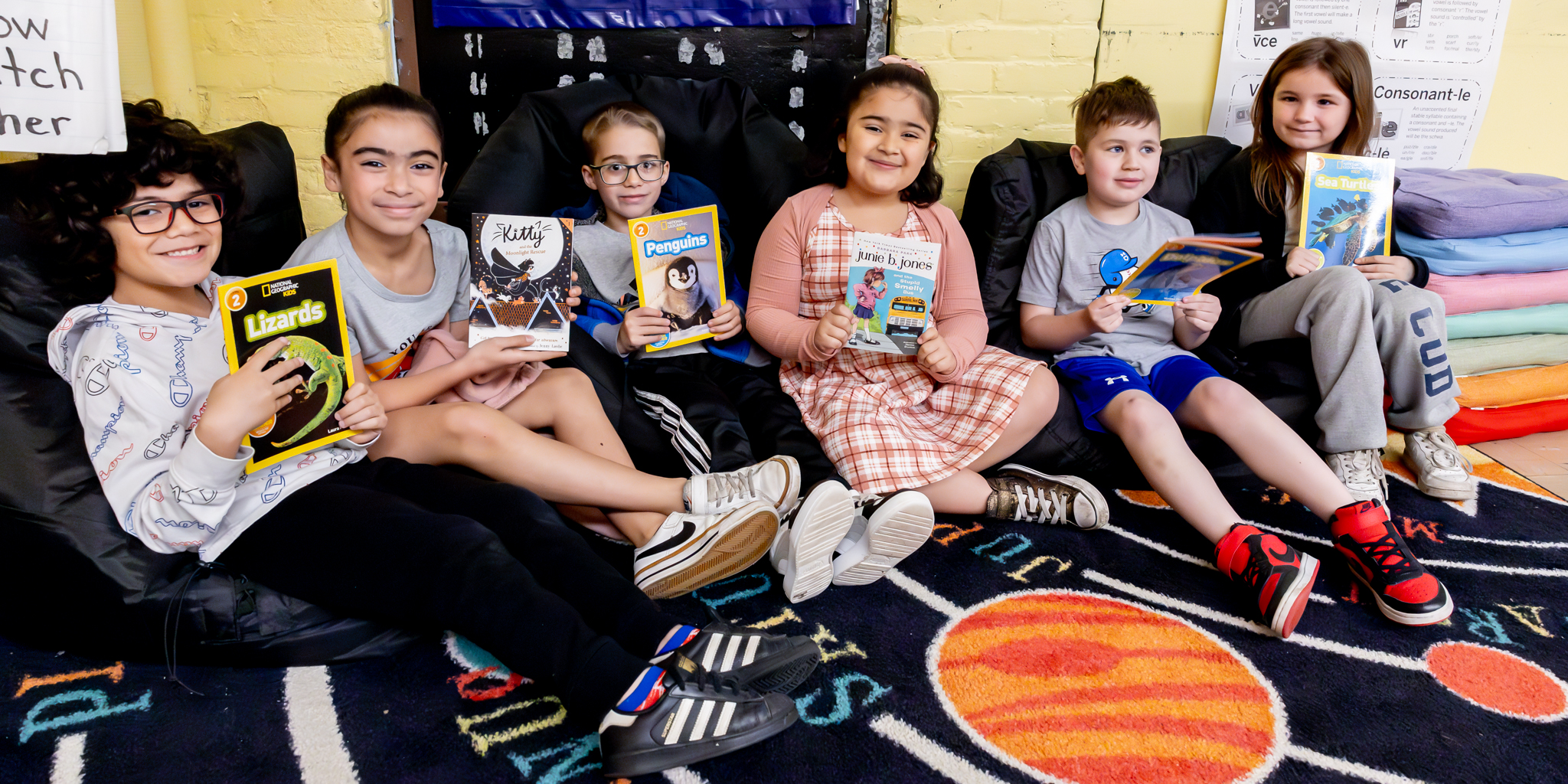 Students hold books in a reading area.