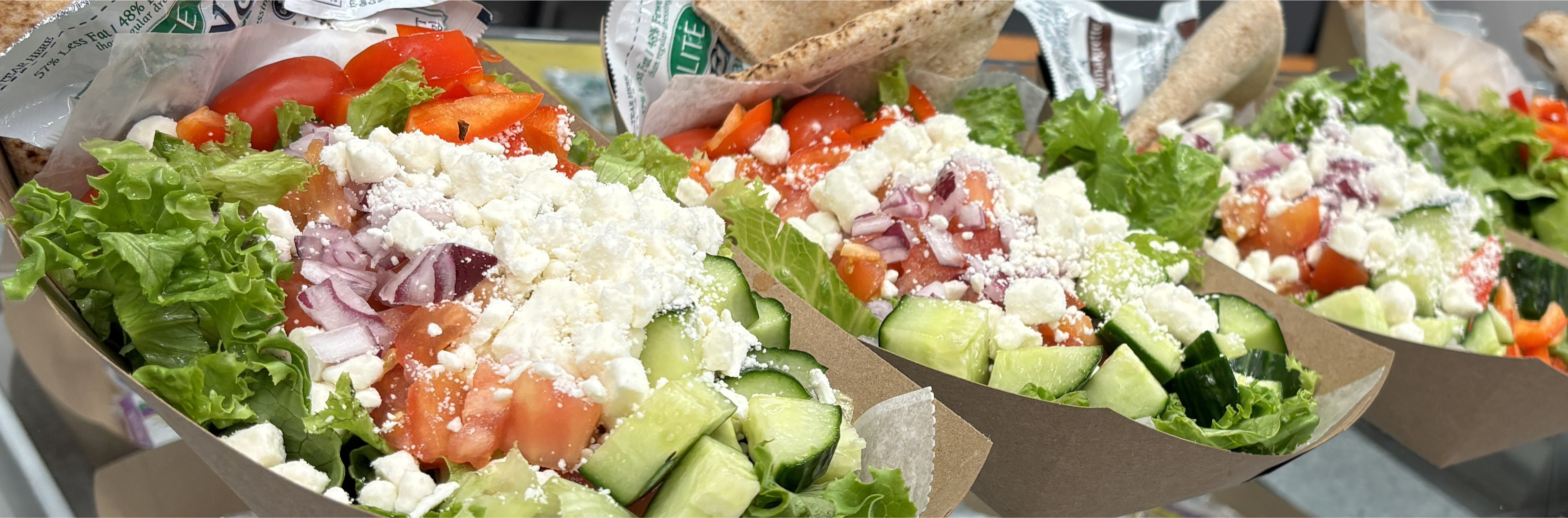 A fresh, colorful salad with leafy greens, cherry tomatoes and cucumber slices, served on a school food line, ready for students to enjoy.