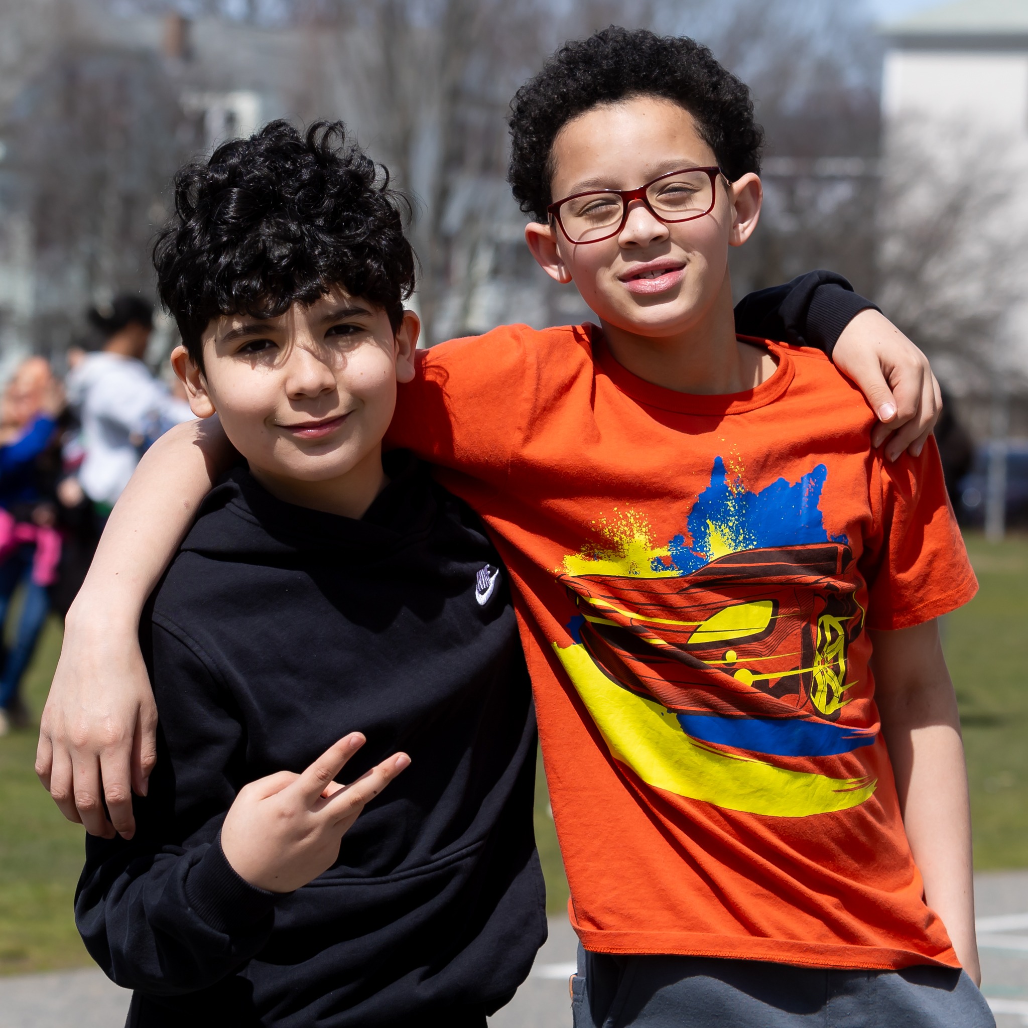 two young boys standing close together outdoors, both smiling and looking at the camera.