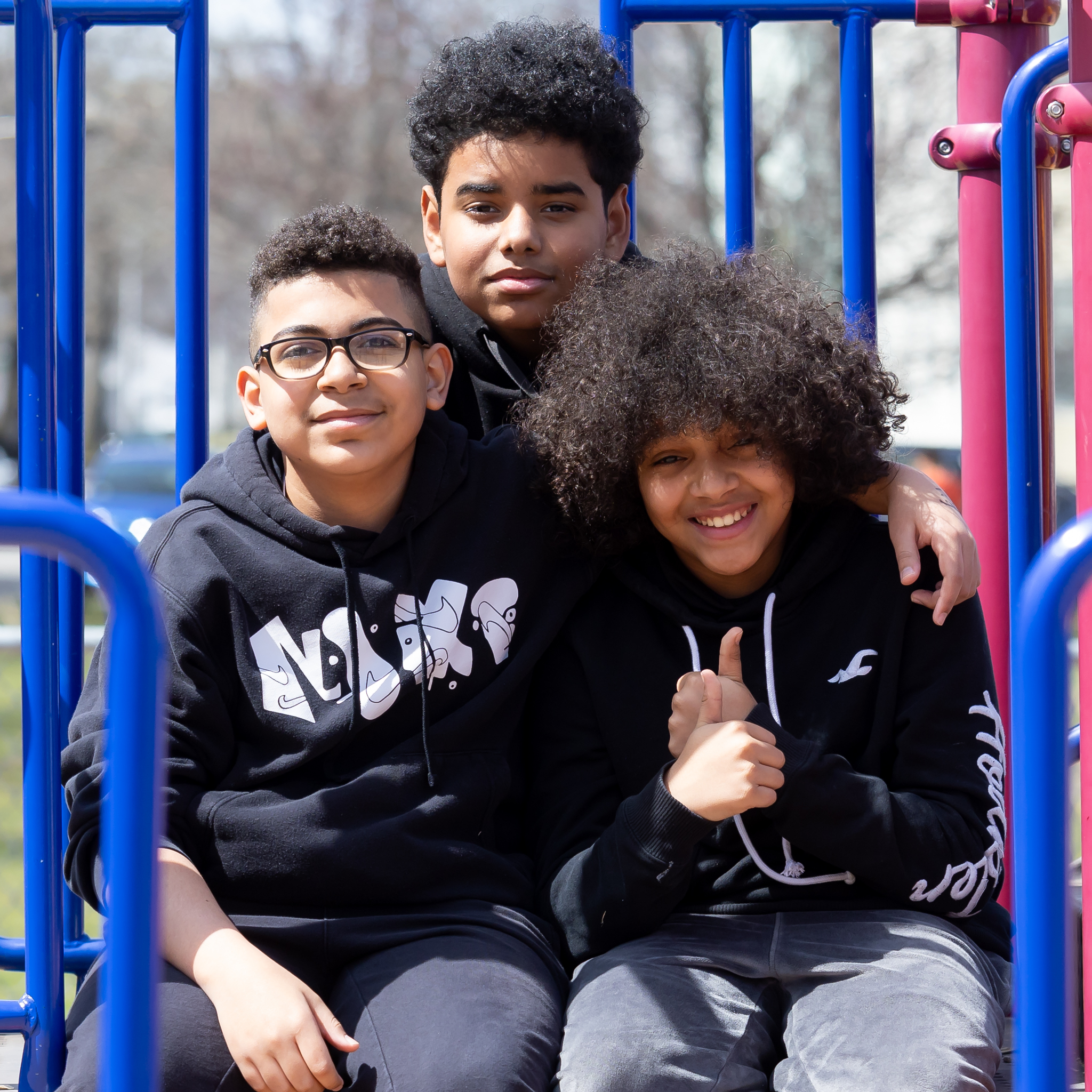 three boys sitting close together on playground equipment, smiling at the camera. 