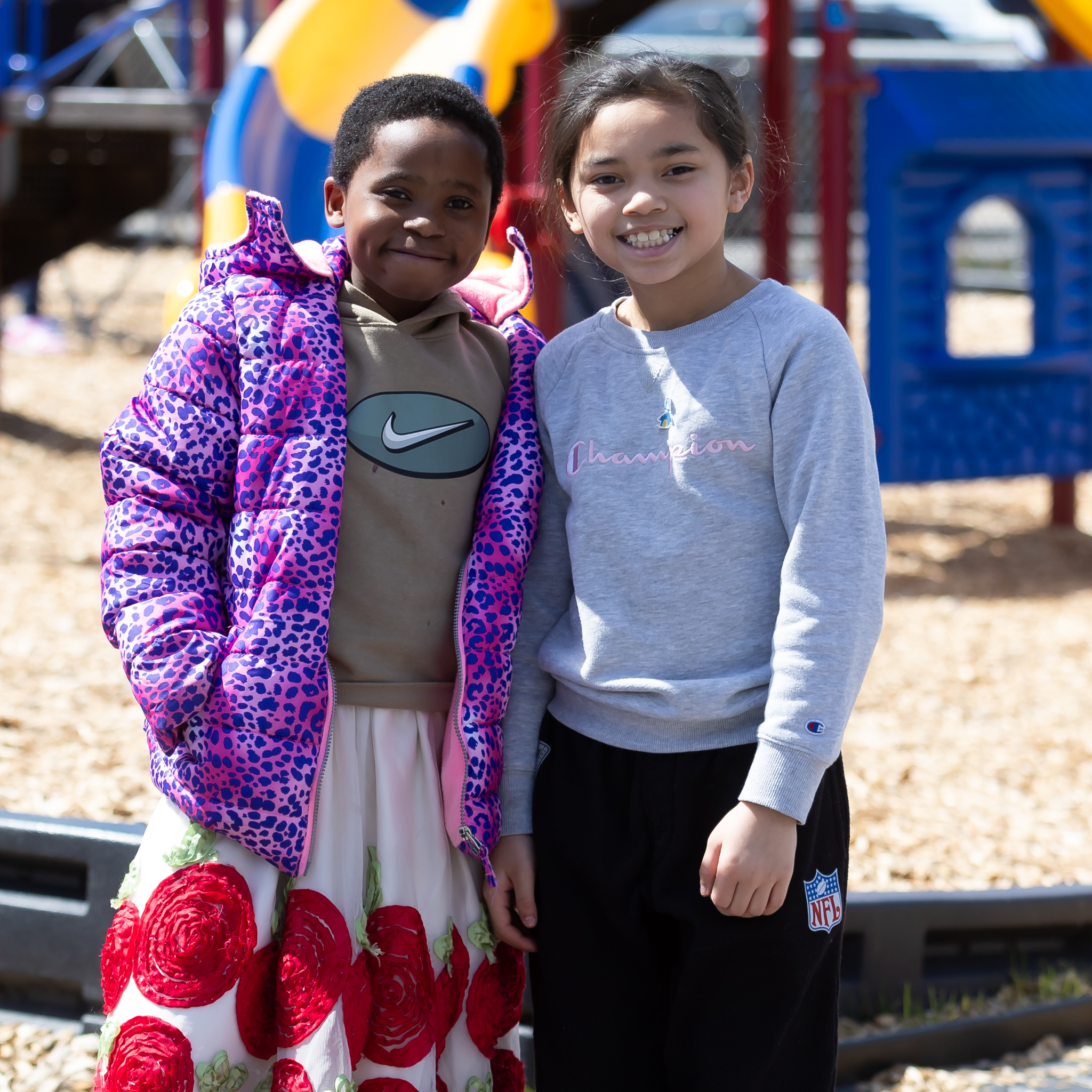 Two young girls standing together and smiling at the camera on a playground