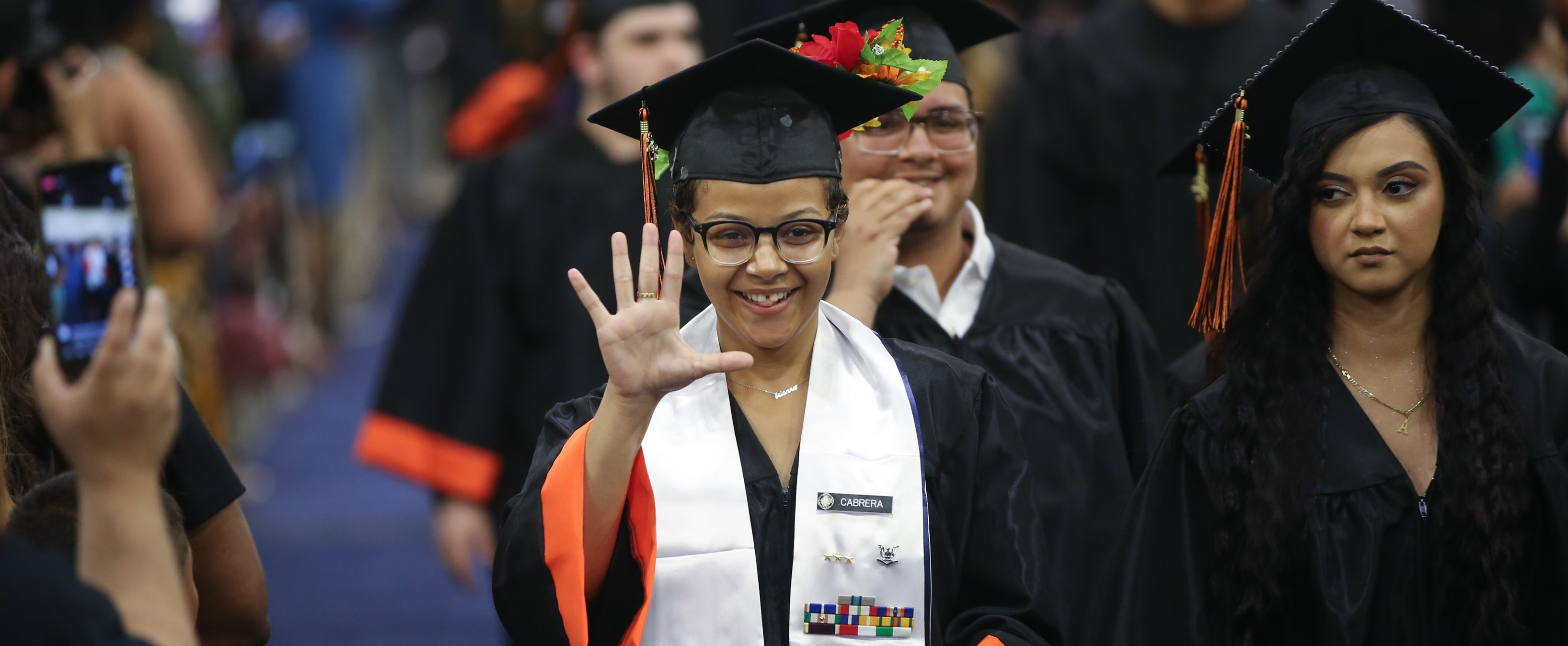 Student in cap and gown waves during graduation ceremony