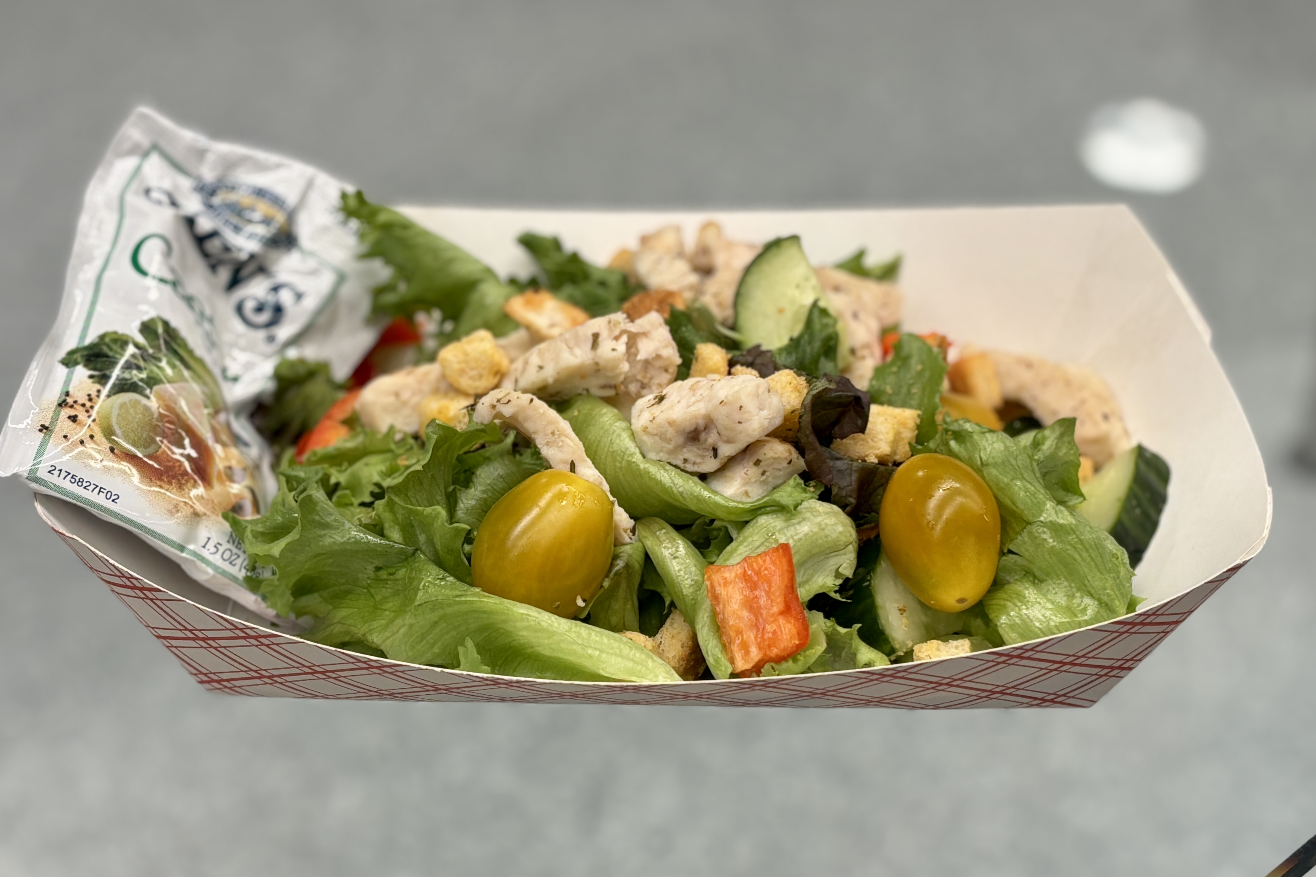 A fresh salad with chicken, tomatoes, and croutons in a paper container.