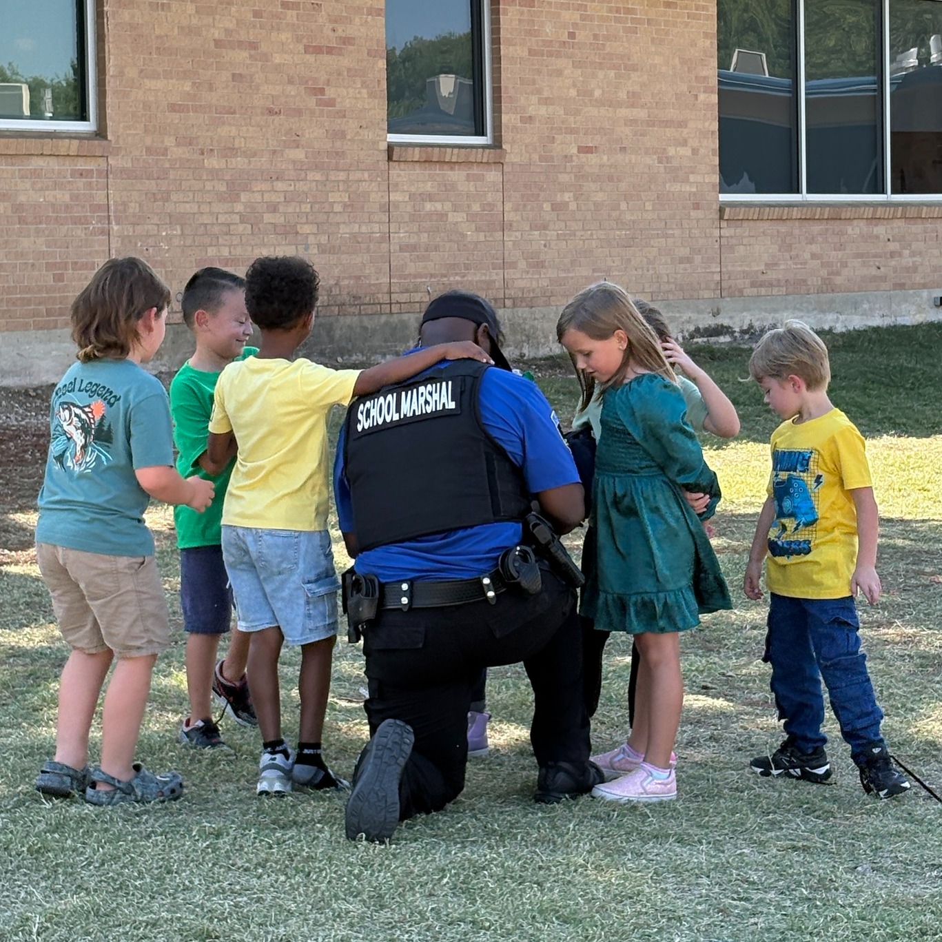 School marshal kneeling with students outside of a school building