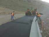 two men smooth asphalt with heavy machinery in the background