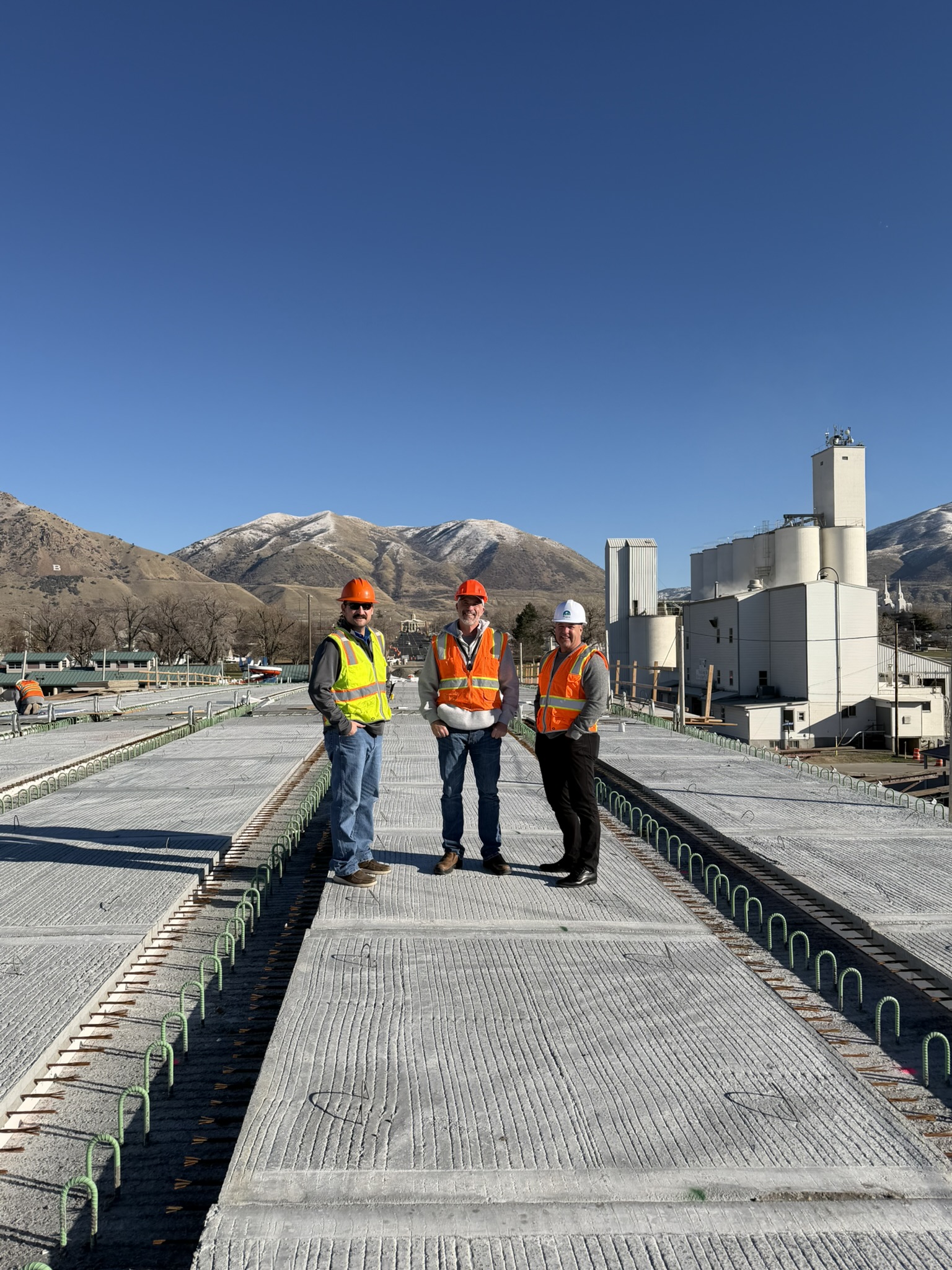 three men in hard hats and reflective vests stand on a concrete base