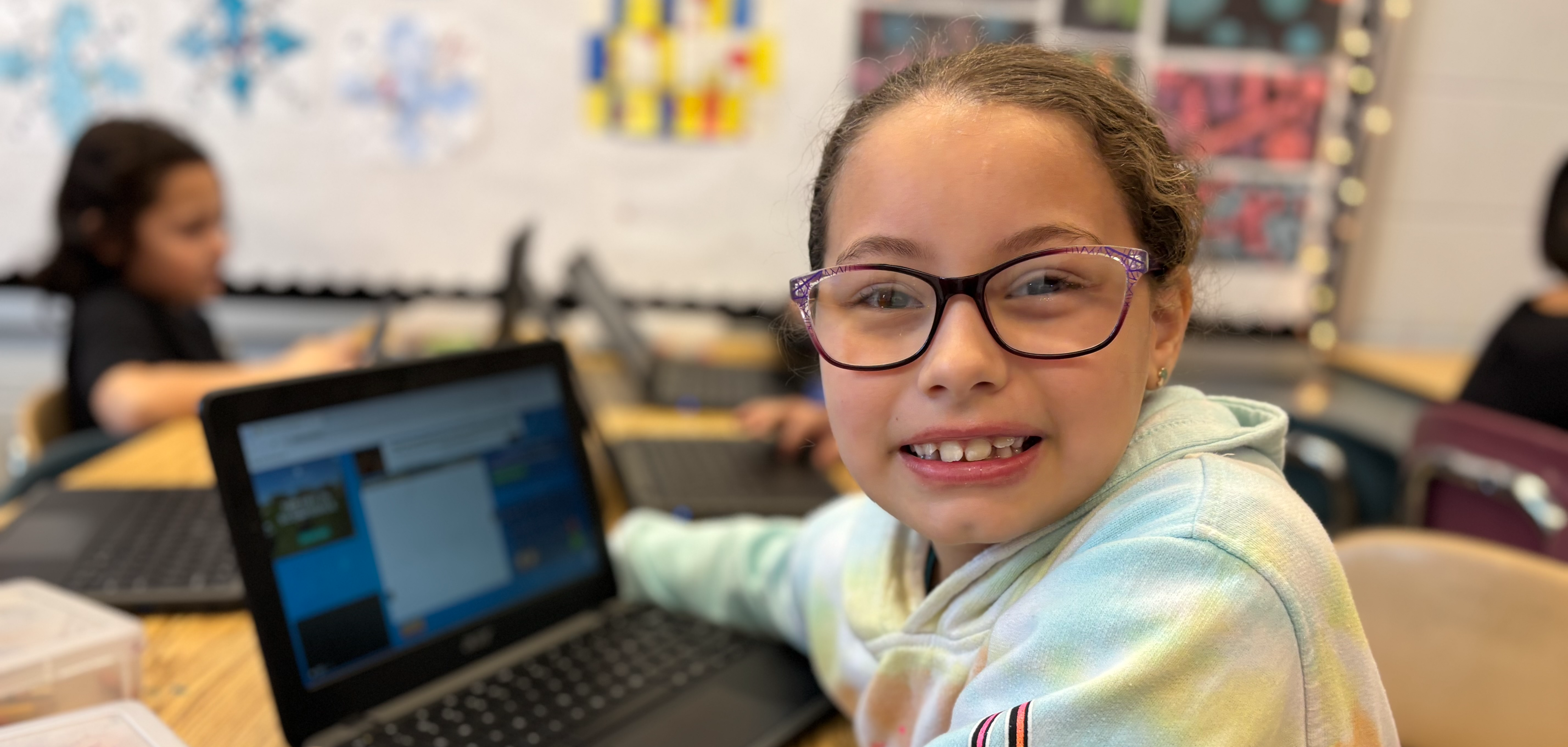 A girl smiling while seated in front of a laptop computer