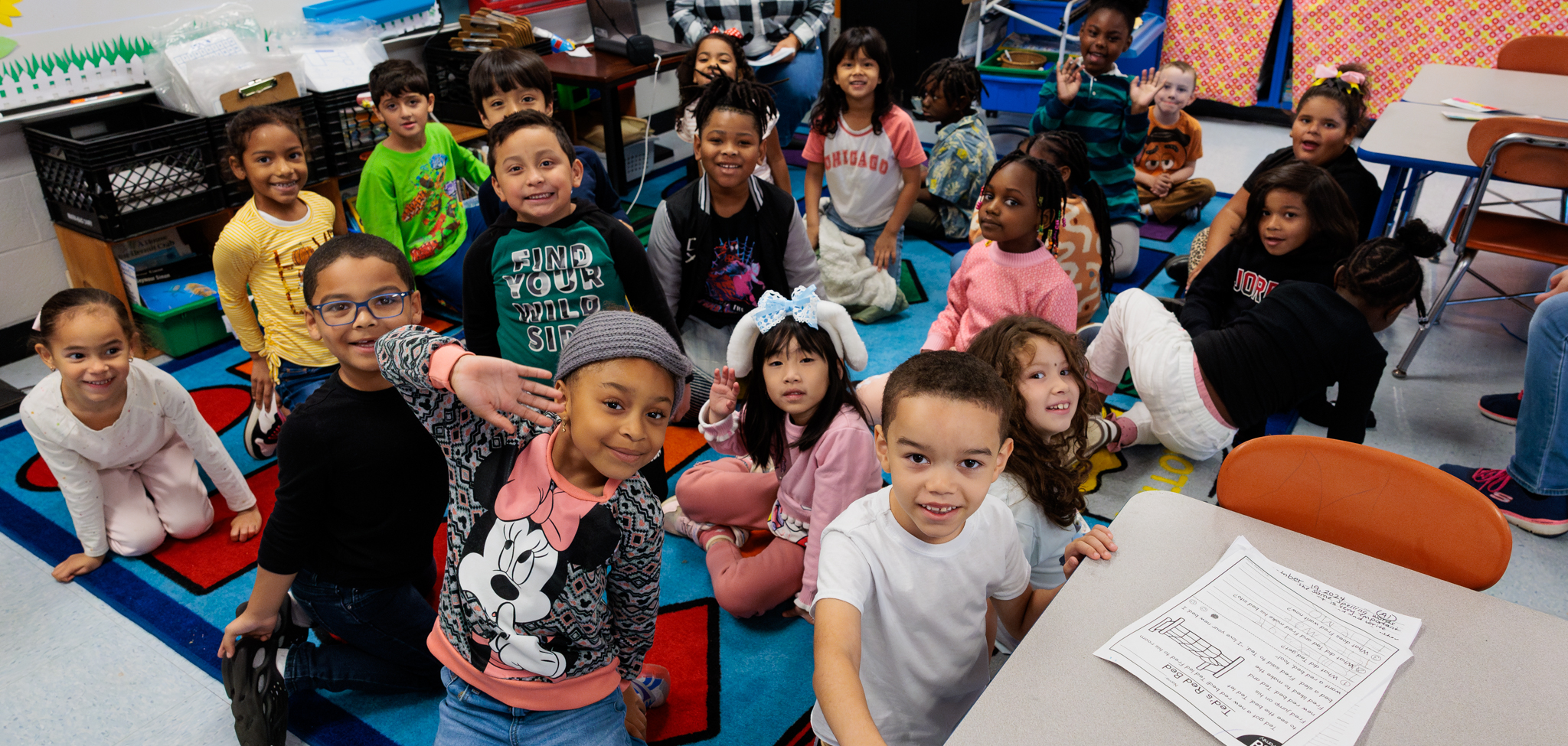 Students in a classroom sit on the rug.