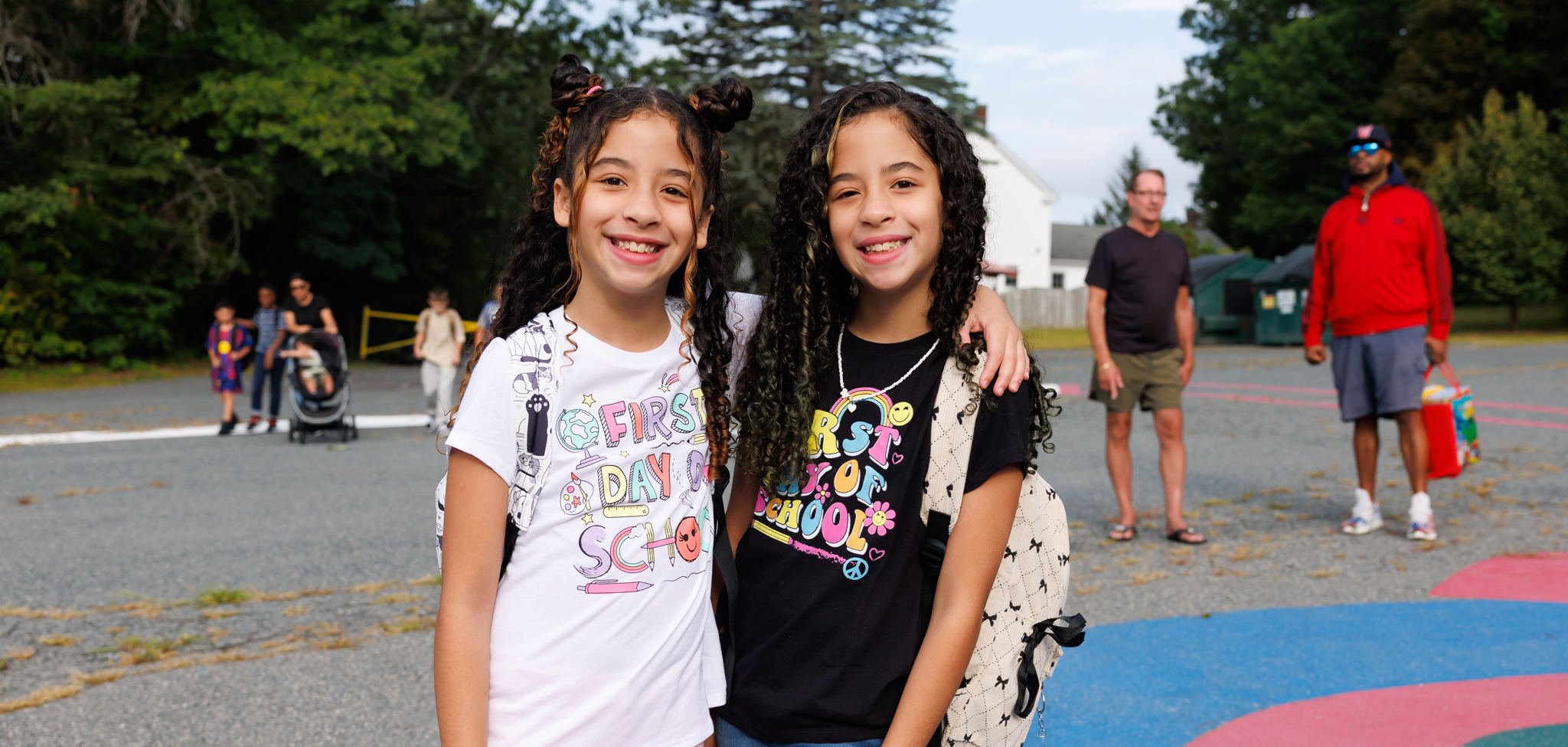 Two students stand together and smile while wearing shirts that say "First Day of School".