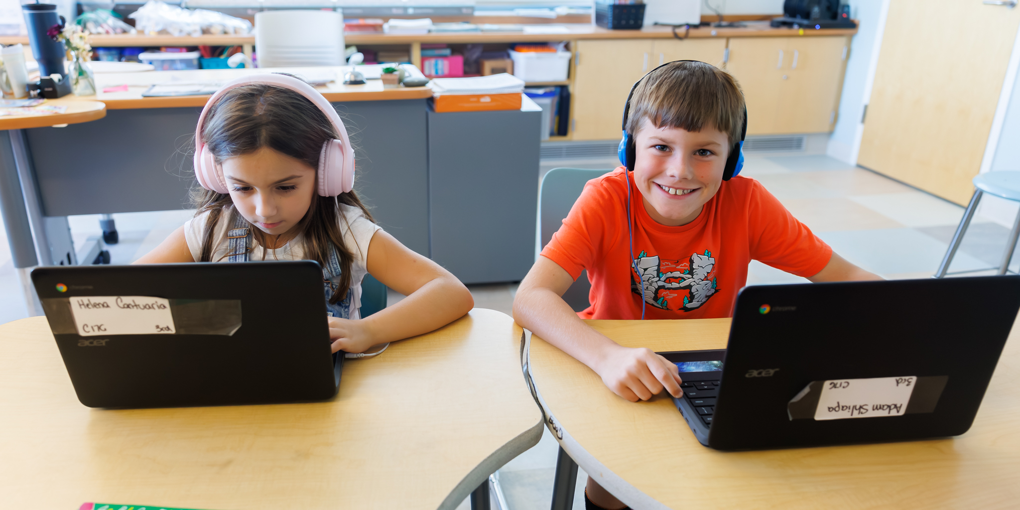 One student works on their computer while another looks at the camera and smiles.