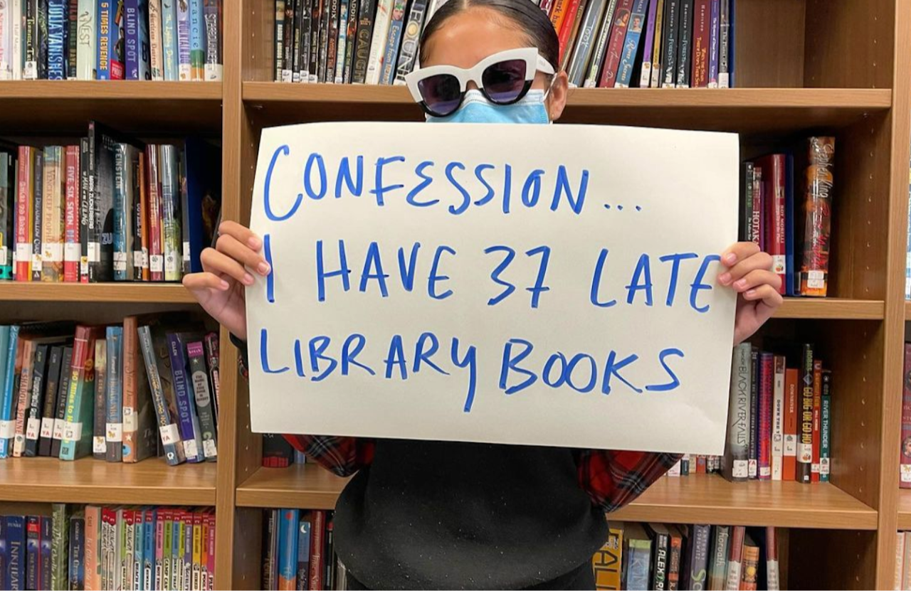 Photo of a student holding a sign that says, "Confession: I have 37 late books."