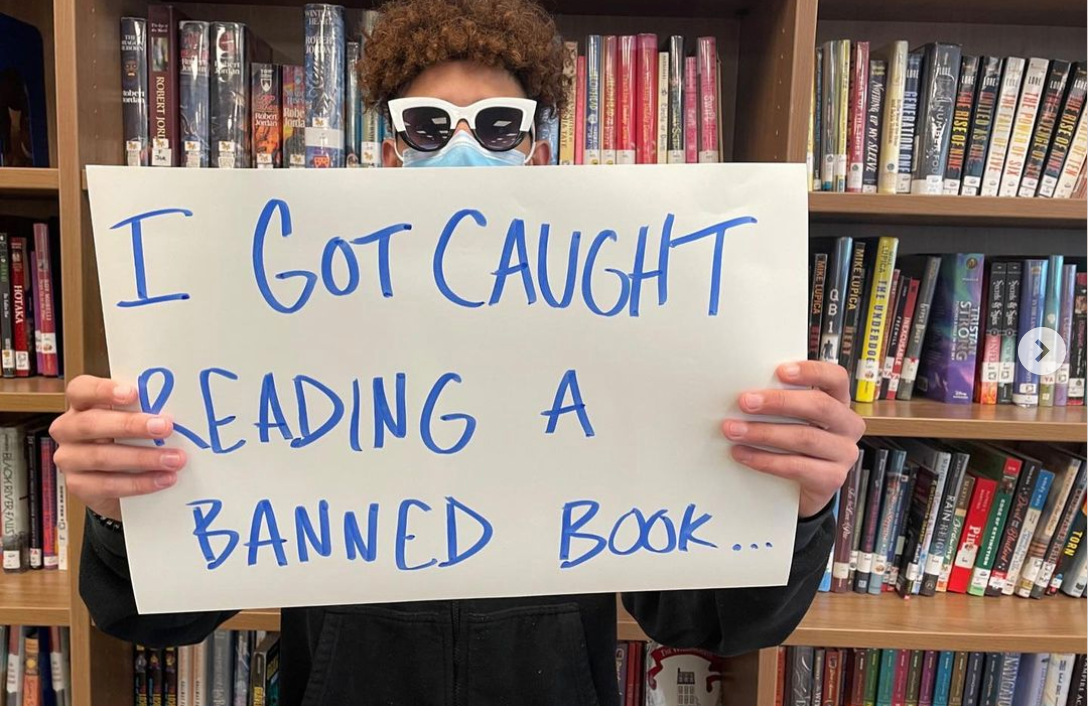 Photo of a student holding a sign that says, "I got caught reading a banned book."