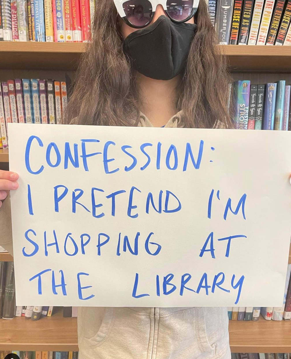 Photo of a student holding a sign that says, "Confession: I pretend I'm shopping at the library."