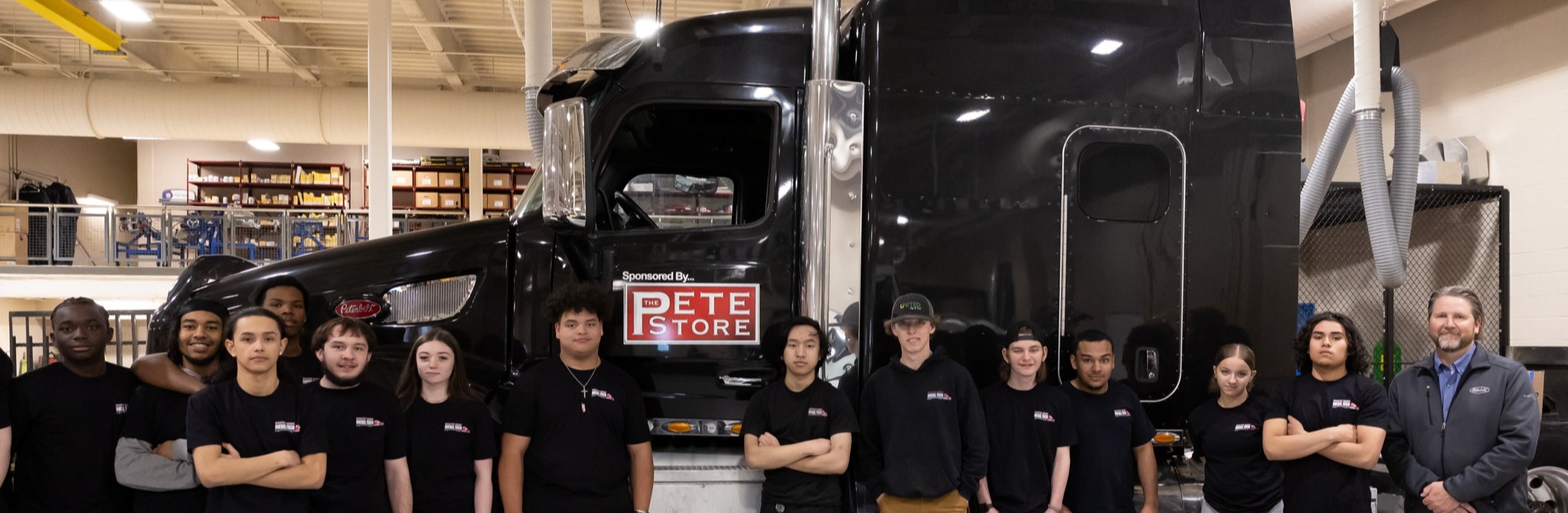 Several students stand in front of a large diesel truck