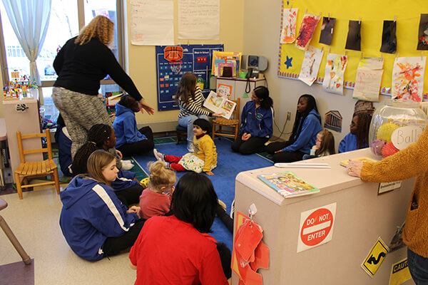 early childhood kids being read to by an adult with students observing