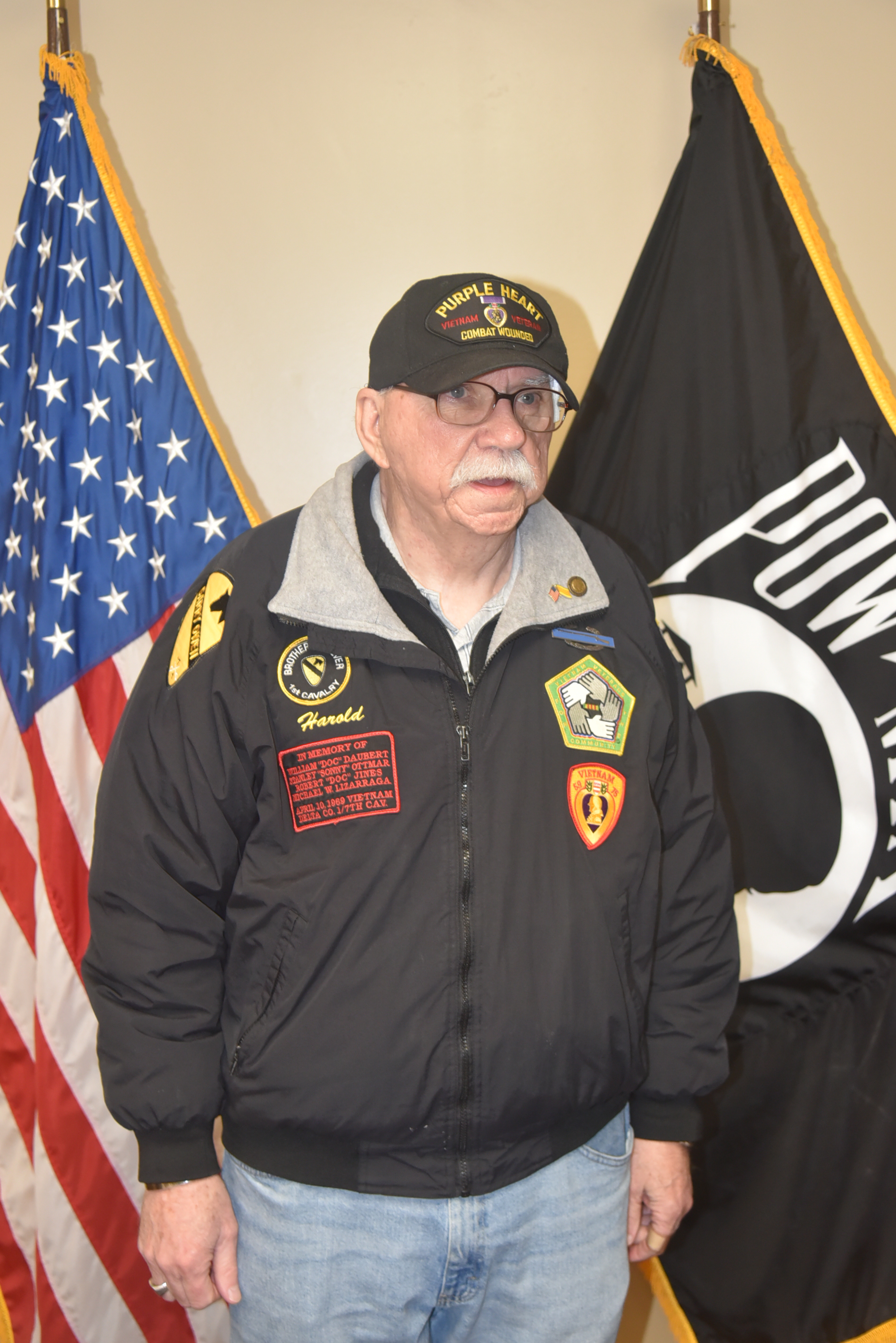 Man in black jacket standing in front of flags.