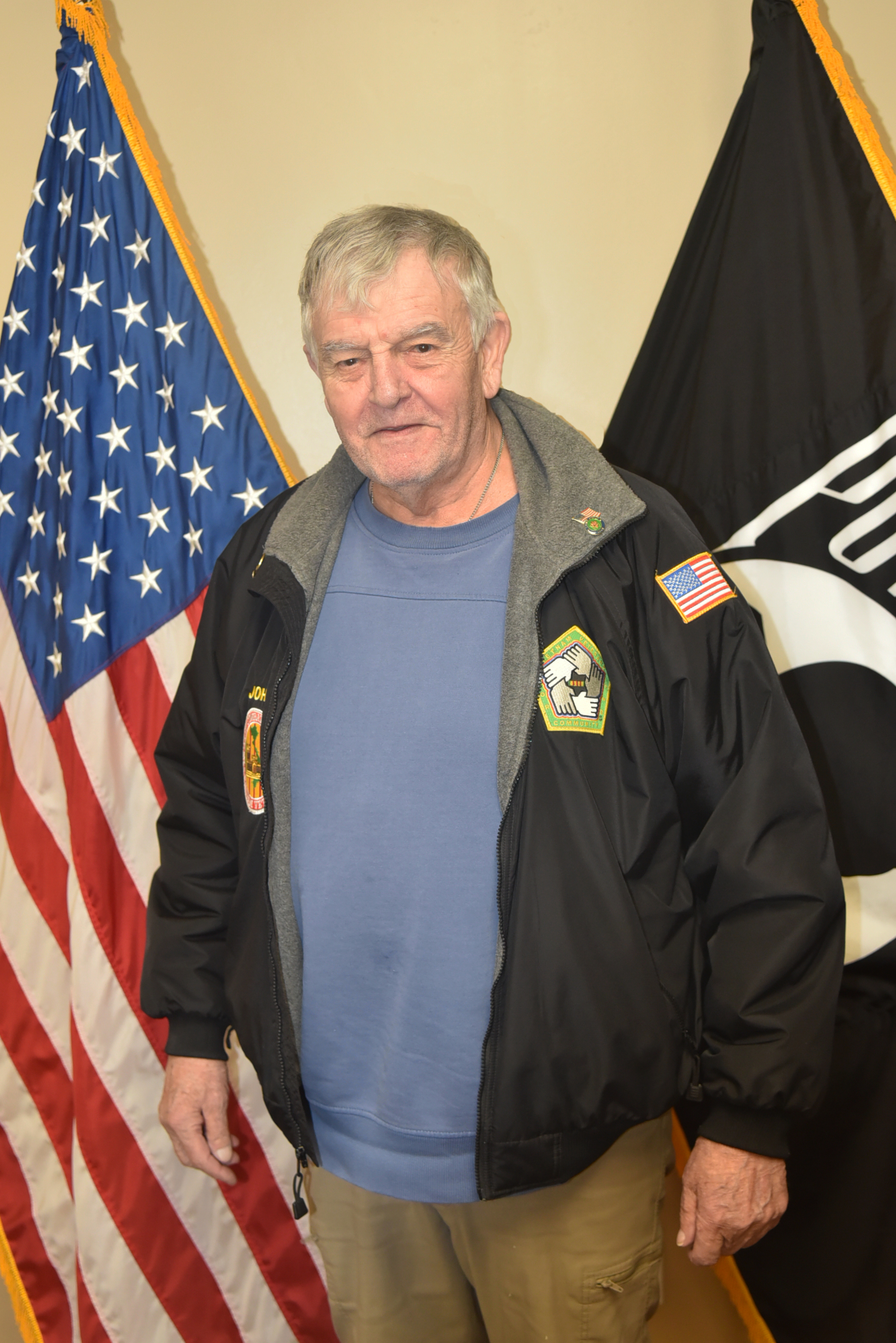 Man in black jacket standing in front of two flags.