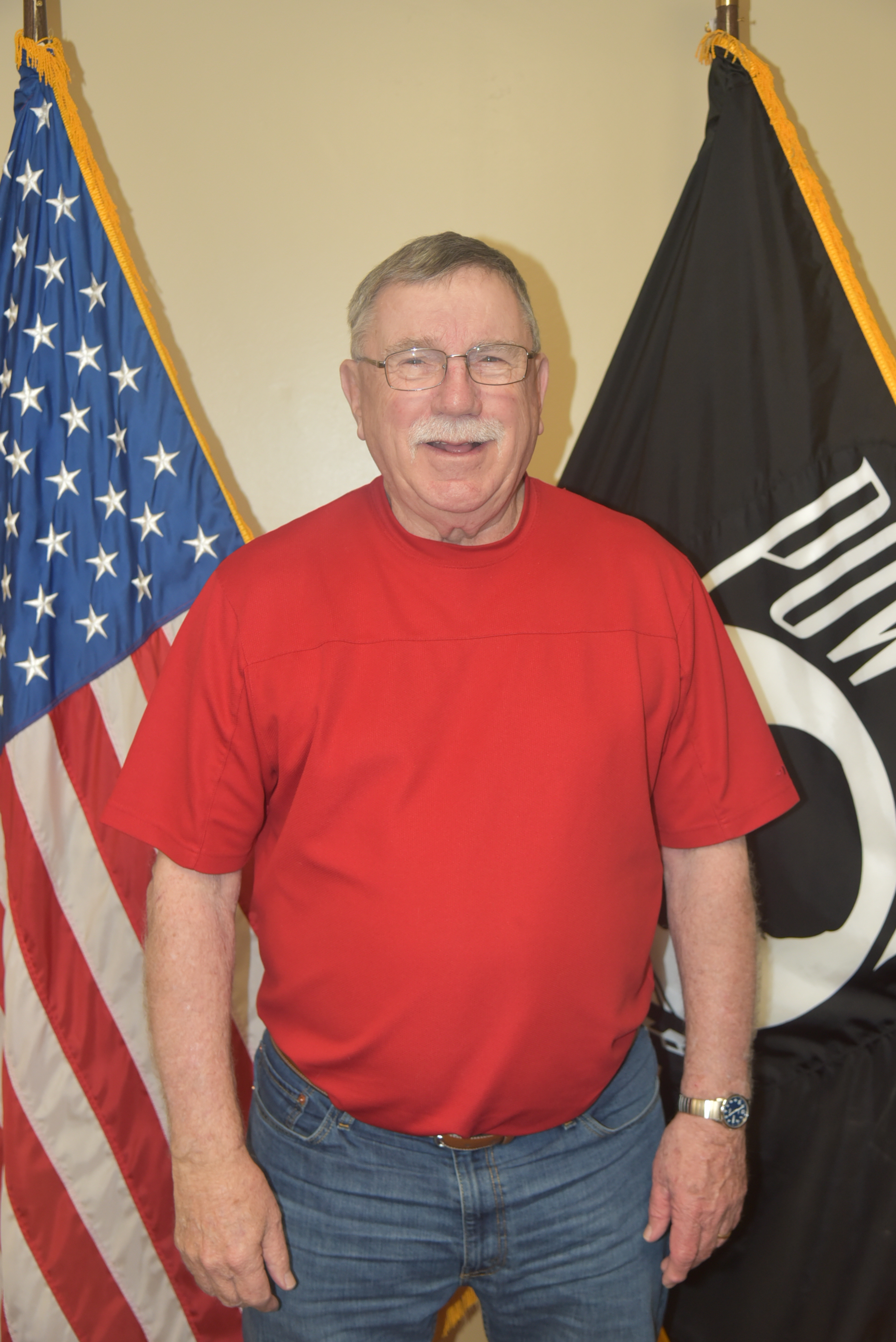 Man with red shirt standing in front of flags.