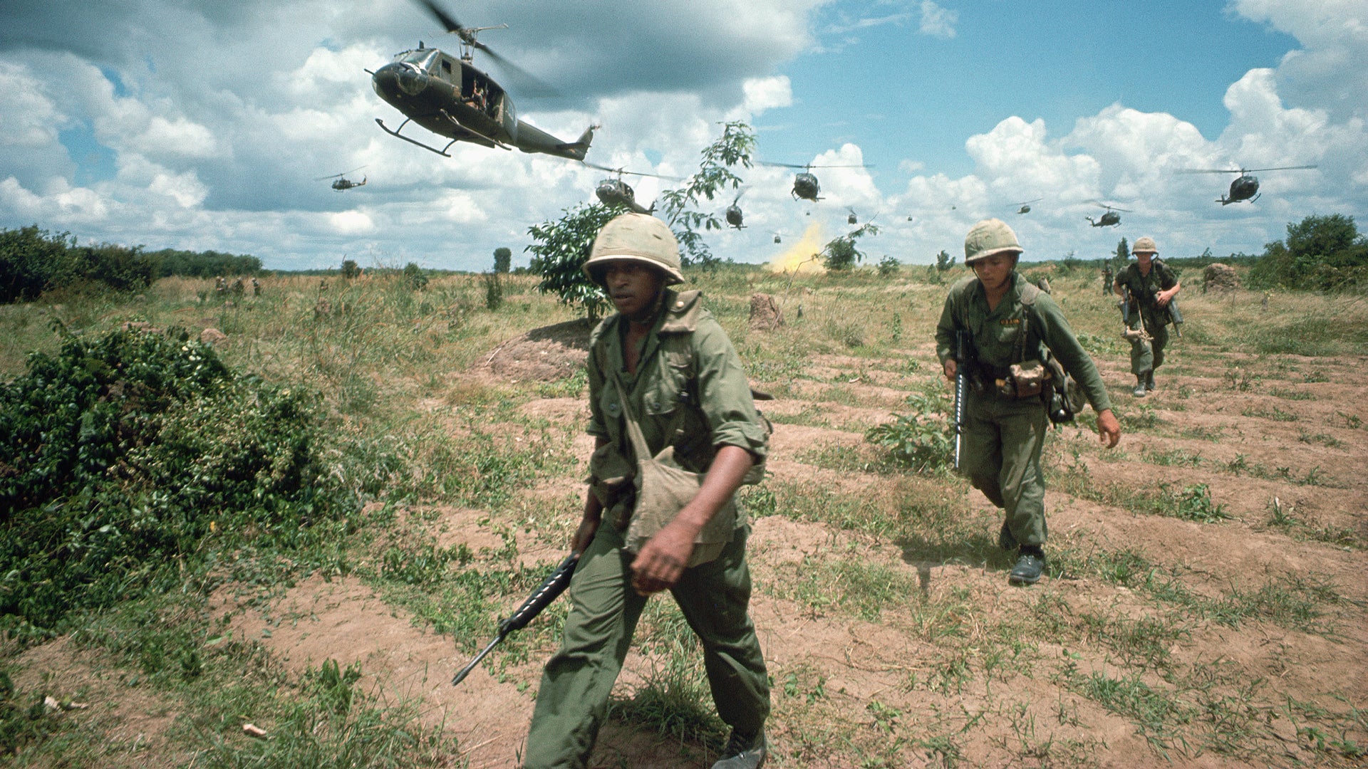 Picture from the war where soldiers are walking with helicopters flying over them.