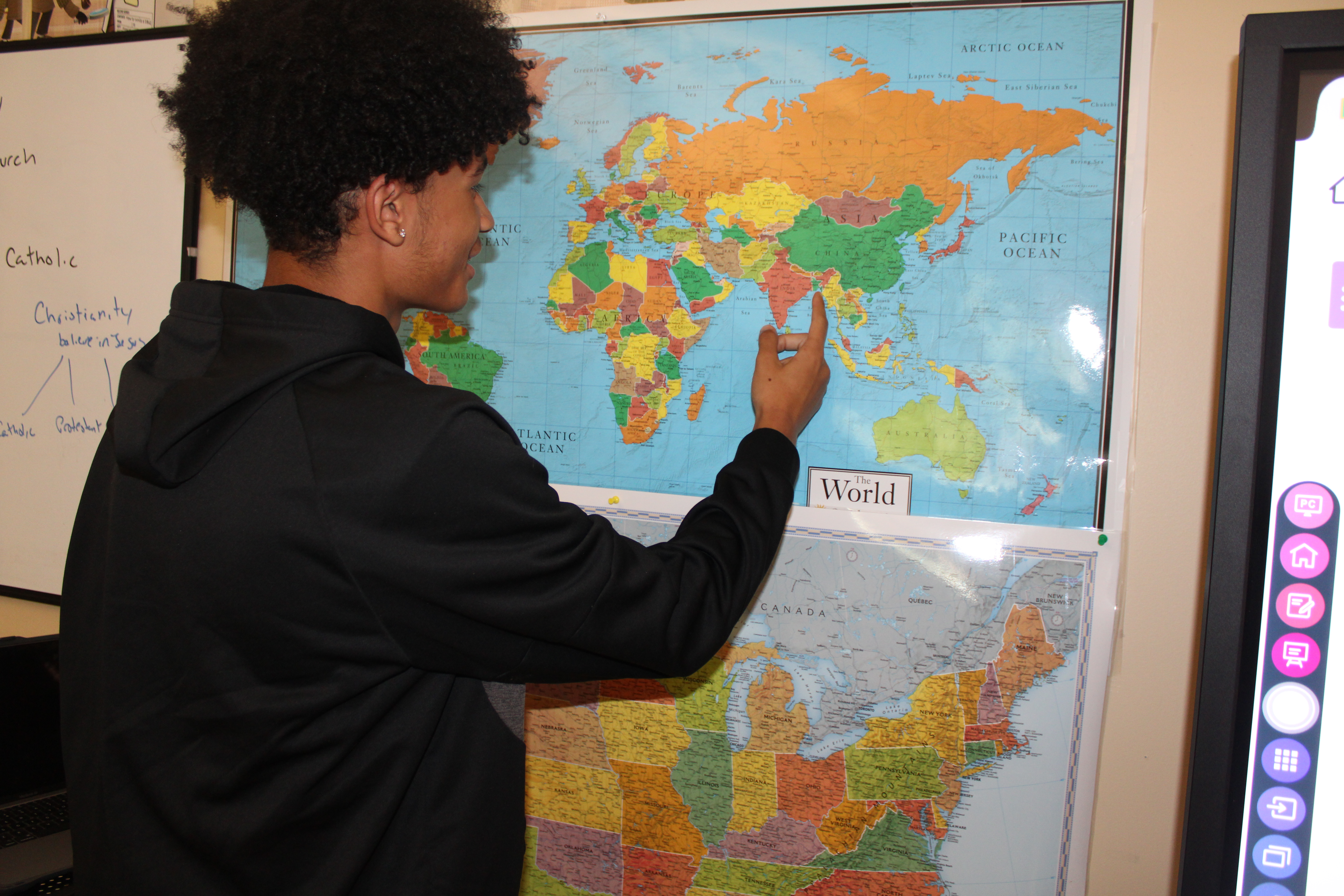 Student pointing out countries on the map in history class.