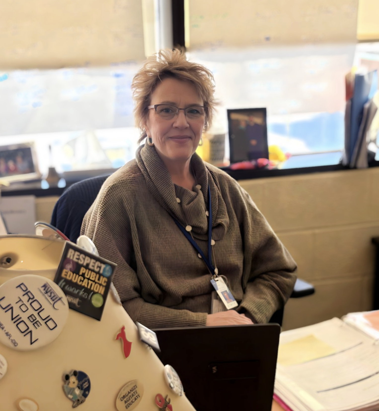 Lori sitting at her desk posing for the camera infront of her office window.
