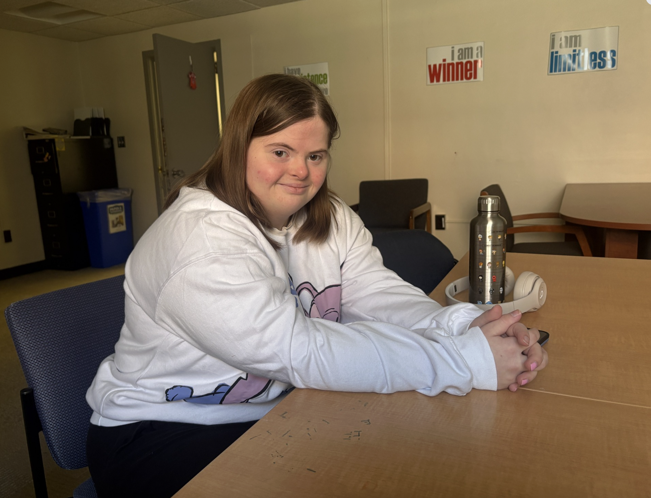 Dani is smiling sitting at a table in the campus classroom.