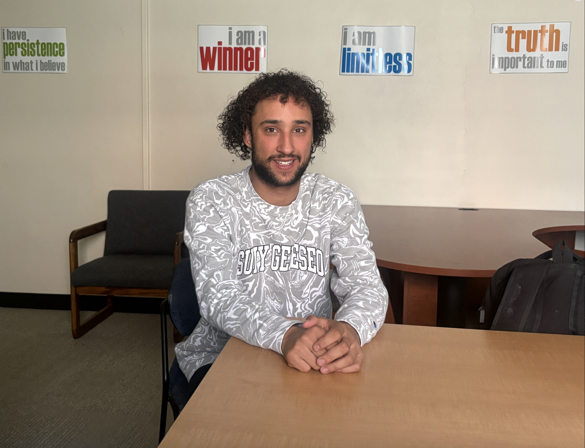 Ty wearing a SUNY Geneseo shirt sitting at a table in a classroom.